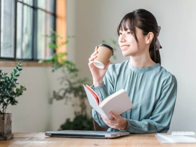 パソコンやスマホを置いて本を読み、デジタルデトックスを心掛けている女性をイメージした画像です。